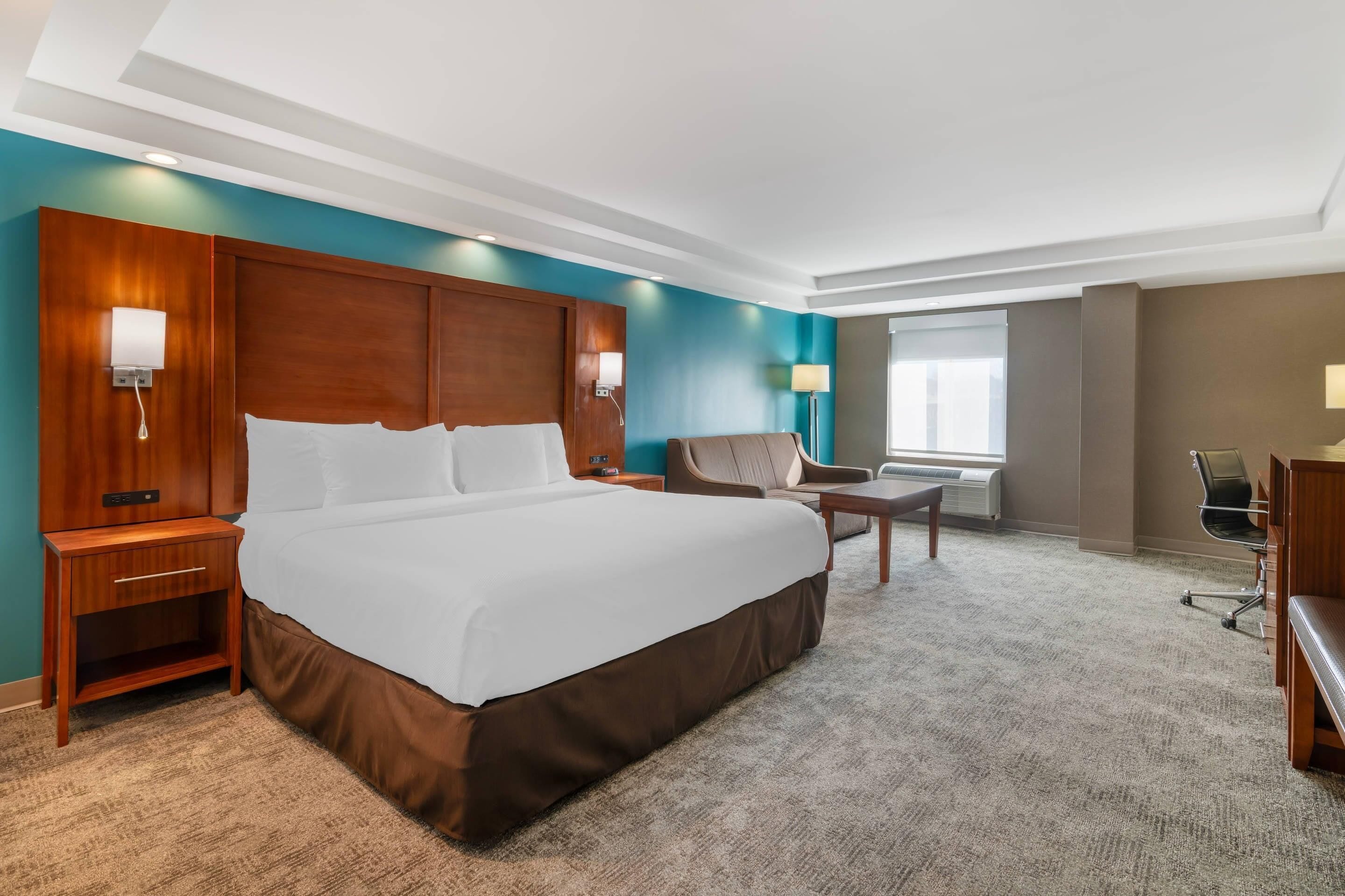 A hotel room with a large bed, bedside tables, a desk, a chair, and a window.