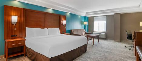 A hotel room with a large bed, bedside tables, a desk, a chair, and a window.