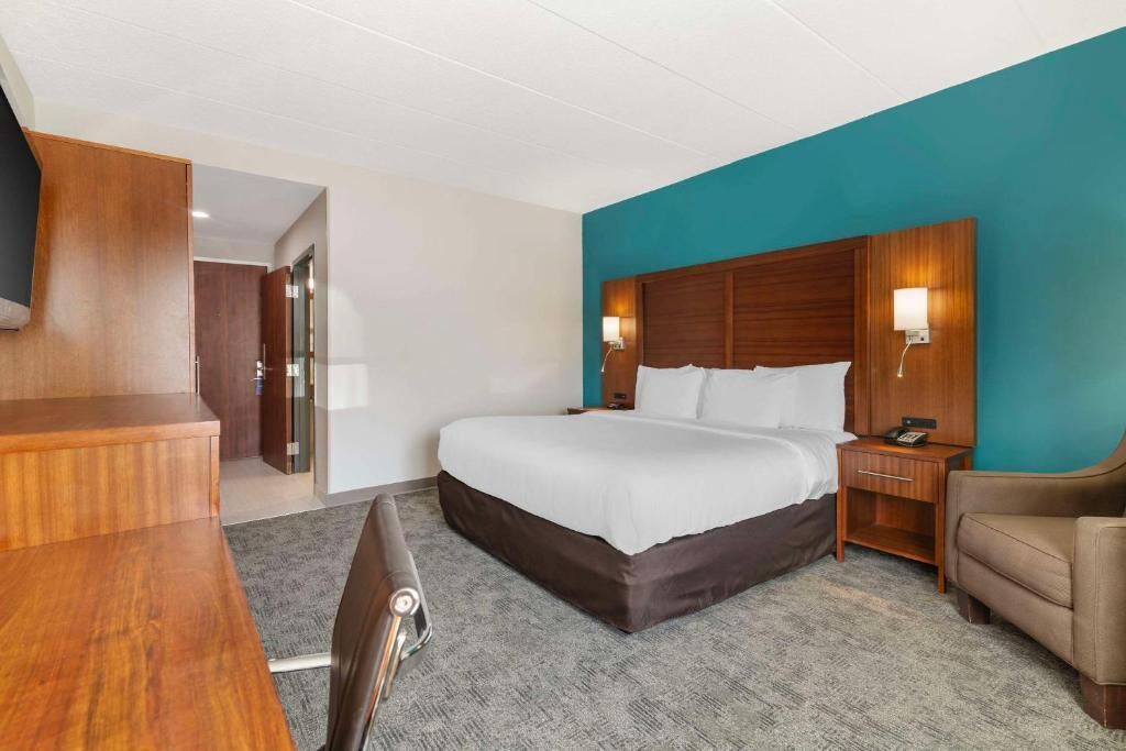 A hotel room with a bed, a desk, a chair, a nightstand, and a TV.