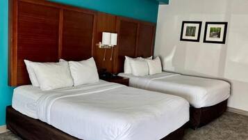 Habitación de hotel con dos camas, cabecero de madera, pared de acento color turquesa y piso alfombrado.