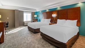 A hotel room with two beds, a desk, a chair, a lamp, and a window.