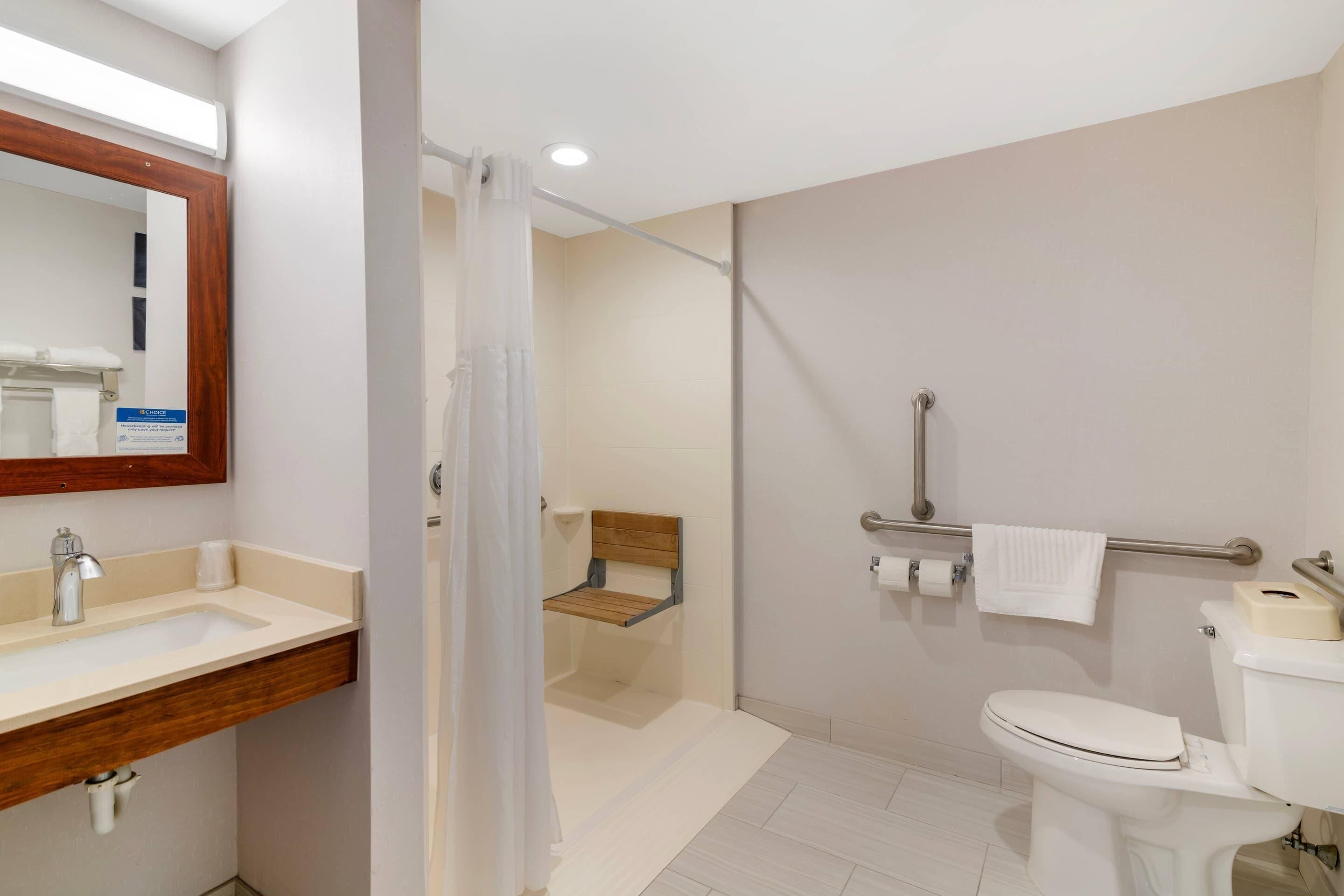 A bathroom with a sink, toilet, shower, and a wooden bench.