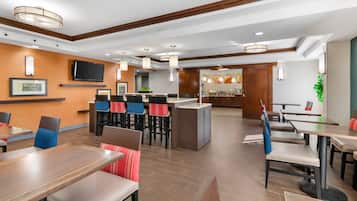 Un restaurant moderne doté d’un plancher en bois, de nombreuses tables, de tabourets de bar et d’un îlot central.