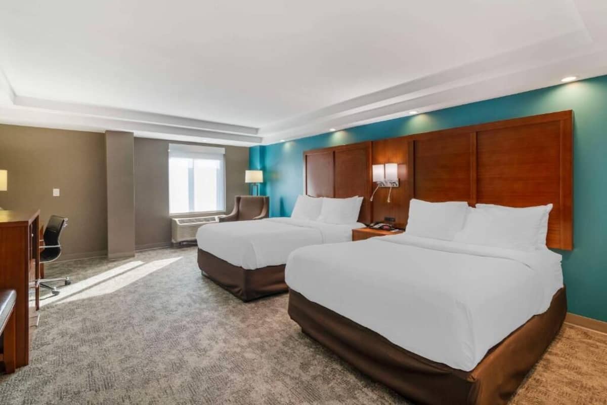 A hotel room with two beds, a desk, a chair, and a window.