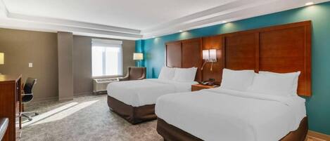 A hotel room with two beds, a desk, a chair, and a window.