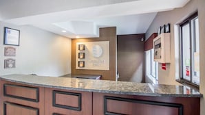 A hotel reception area with a granite counter, wooden cabinets, and a wall-mounted sign that reads "Comfort Inn". - Quality Inn Corning (Corning)