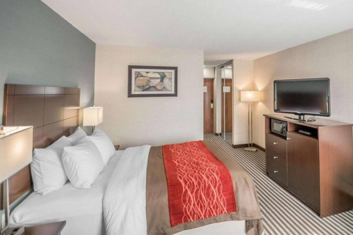 Habitación de hotel con cama, lámparas de noche, televisión, escritorio con computadora y un cuadro en la pared.
