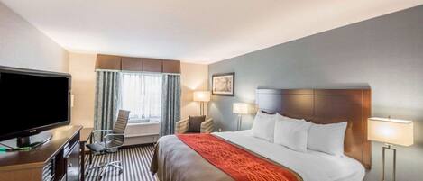 Habitación de hotel con una cama grande, un televisor sobre un mueble de madera, un escritorio con una silla y una ventana con cortinas.