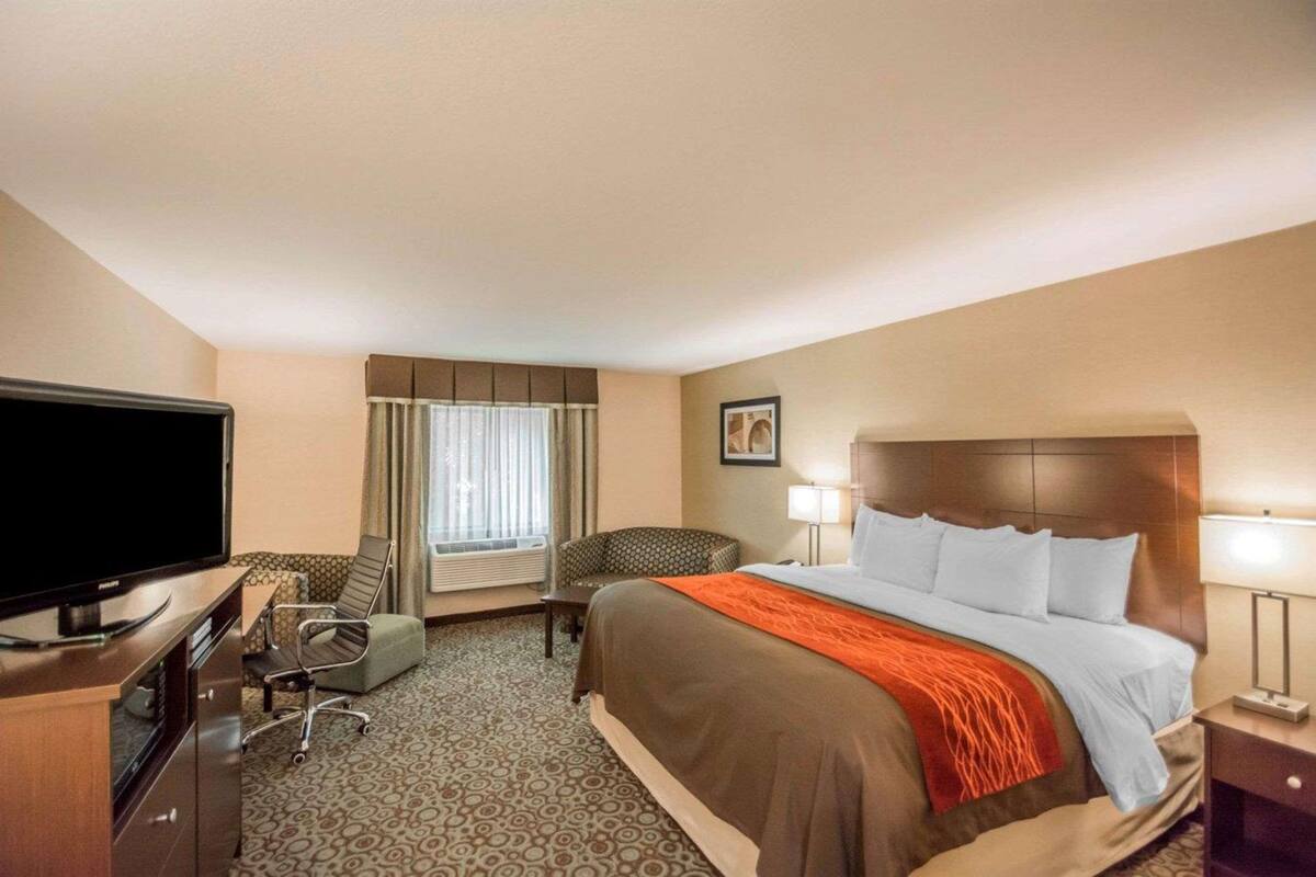 Habitación de hotel con cama, televisor, escritorio, silla y ventana con cortinas.