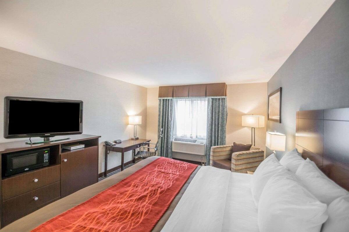 Habitación de hotel con cama, televisión, escritorio, silla y ventana con cortinas.