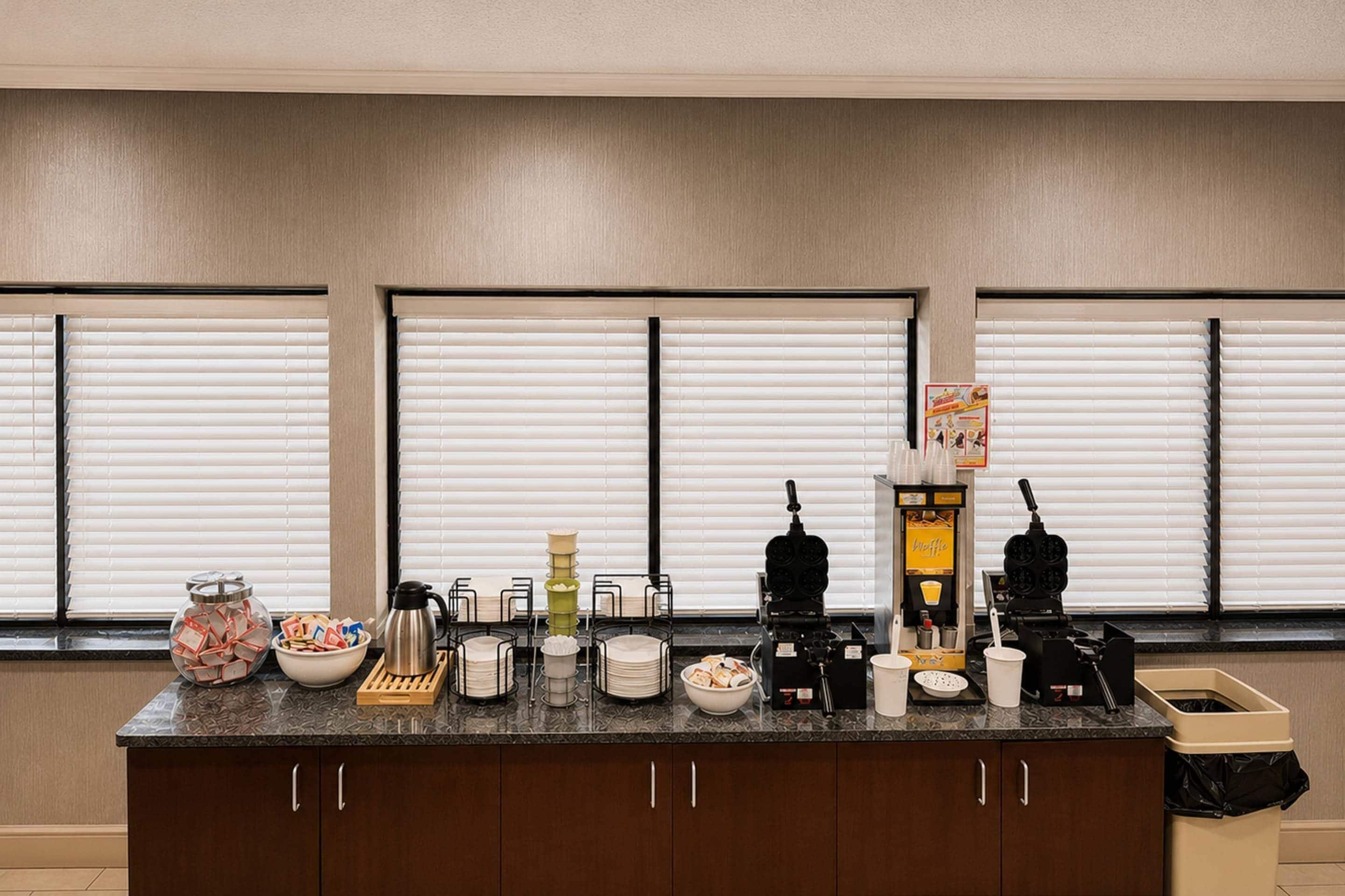 Una encimera de cocina con varios electrodomésticos y objetos, como un waffler, una cafetera y un cubo de basura.