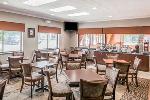 Un restaurante con varias mesas y sillas, una zona de cocina con máquinas de café y grandes ventanales con persianas.