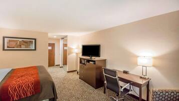 A hotel room with a bed, a desk, a chair, a television, and a lamp.