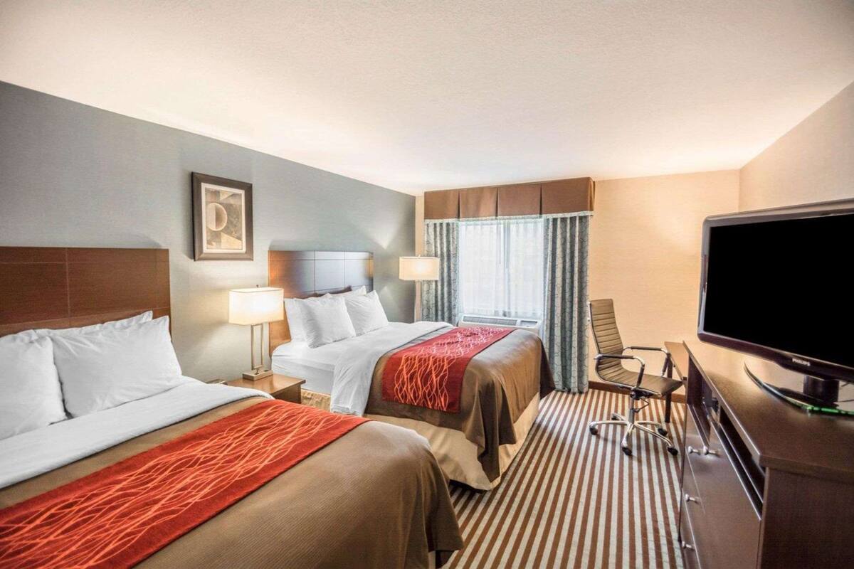 Habitación de hotel con dos camas, un escritorio, televisor y ventana con cortinas.