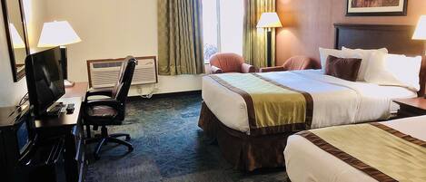 A hotel room with a bed, two chairs, a desk with a computer, and a TV.
