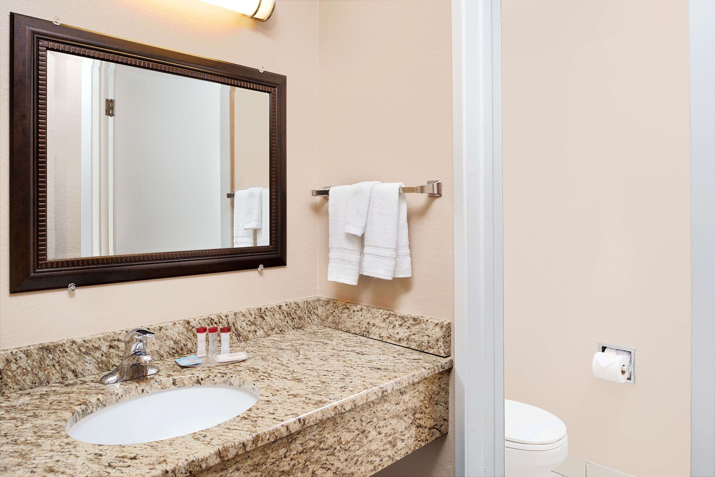 A bathroom with a granite countertop sink, a mirror, and a toilet.