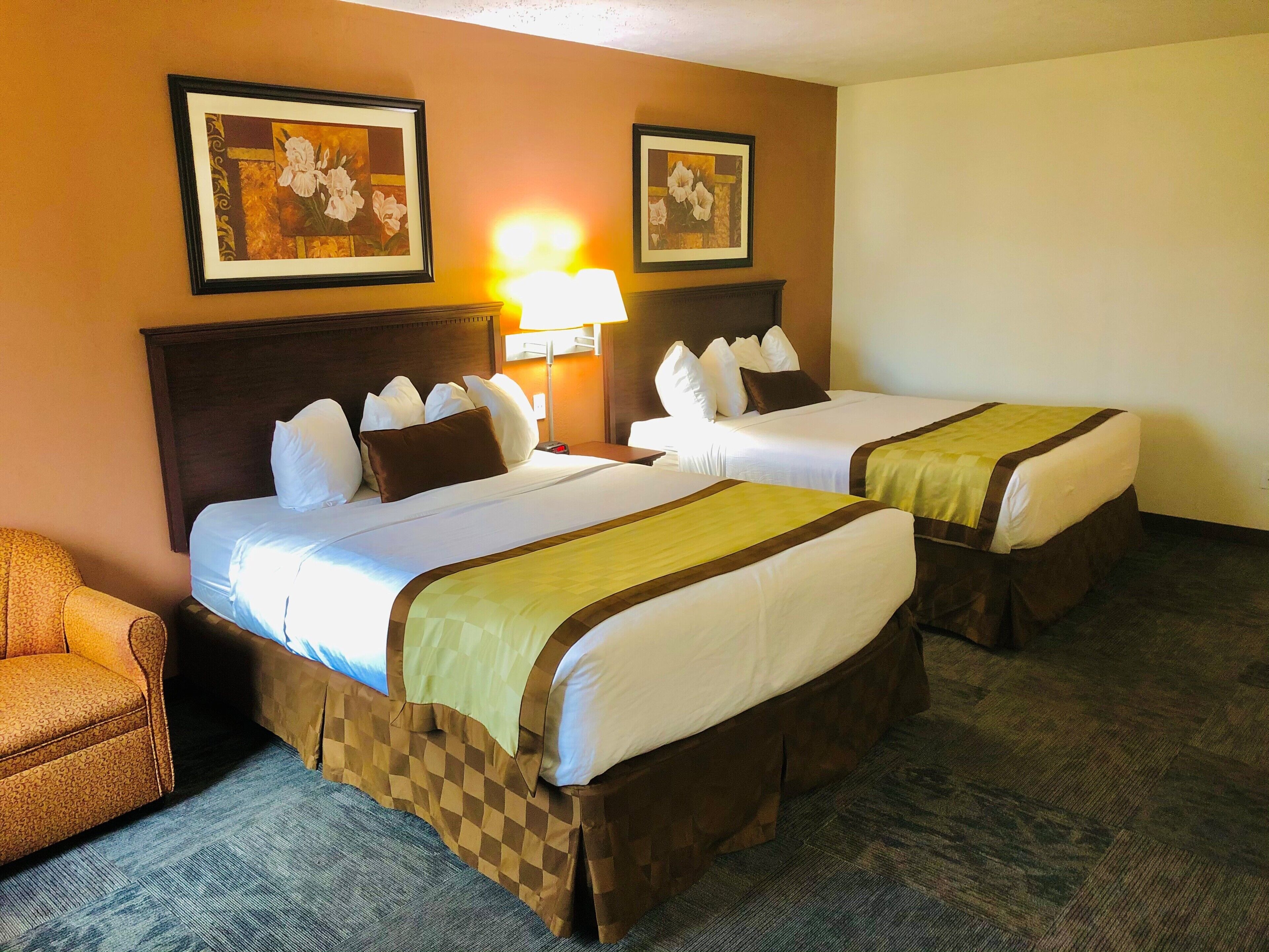 A hotel room with two beds, a chair, and two framed pictures on the wall.