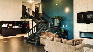 A modern living room with a dark wooden staircase, a beige sofa, and a flat-screen TV mounted on the wall.
