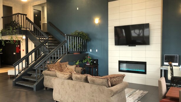 A modern living room with a staircase, a flat-screen TV, a fireplace, and a sofa.