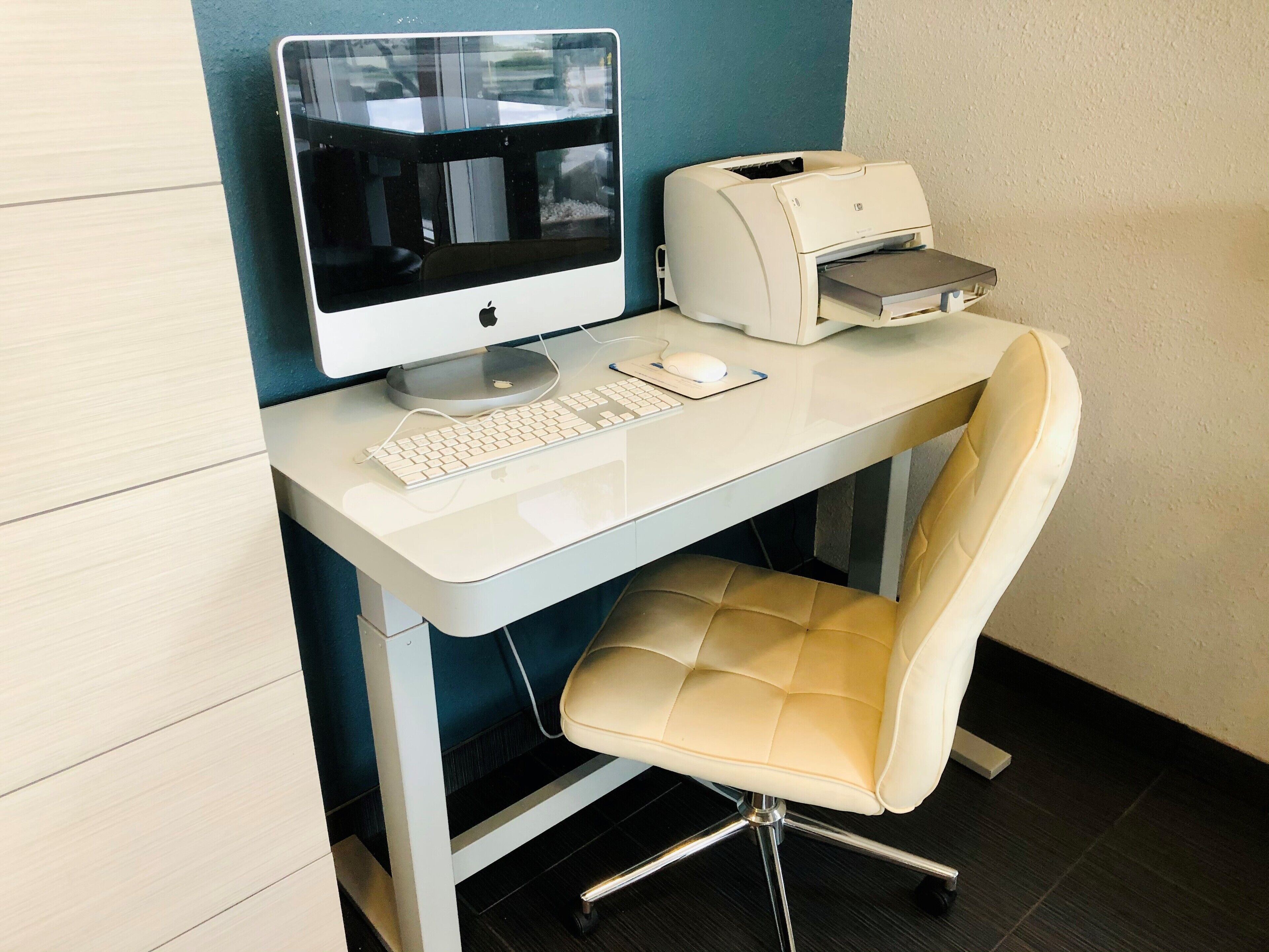 A modern office desk with a desktop computer, a printer, and a cushioned chair.