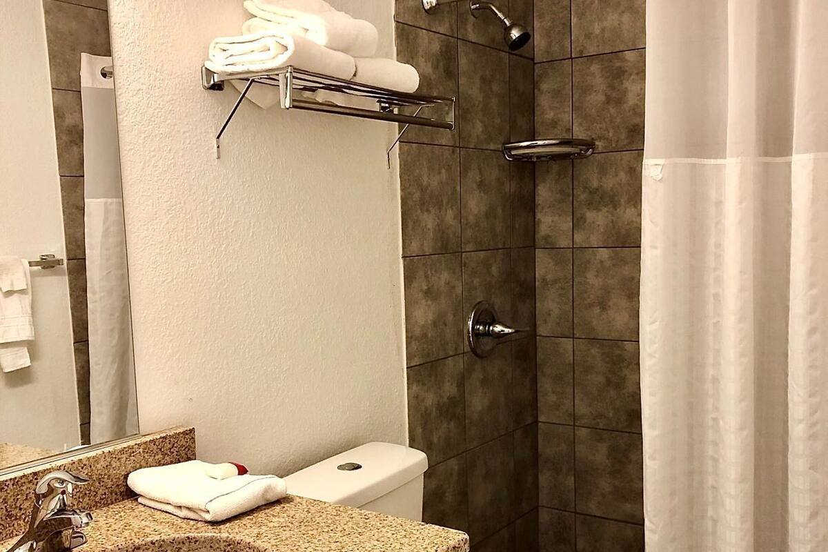 A bathroom with a granite countertop sink, a toilet, a shower with a glass door, and a towel rack with towels.
