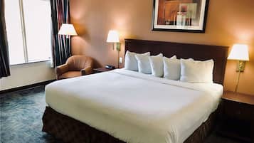 A hotel room with a large bed, two bedside lamps, a chair, and a framed picture on the wall.