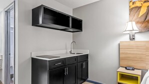 A modern kitchen with black cabinets, a stainless steel sink, and a wooden sideboard with a yellow shelf.