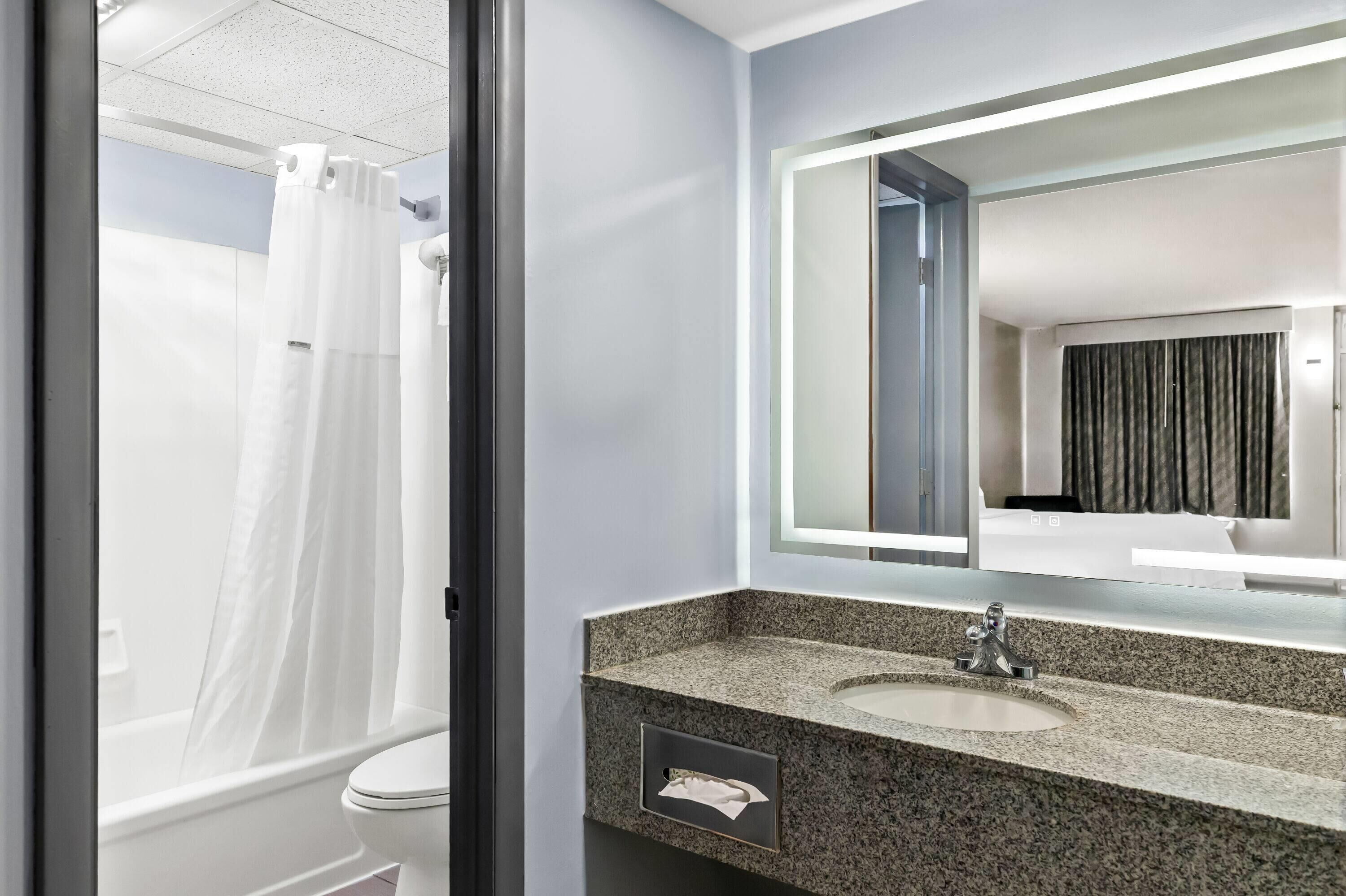 A bathroom with a white toilet, a granite sink, a mirror with a light, and a shower curtain.