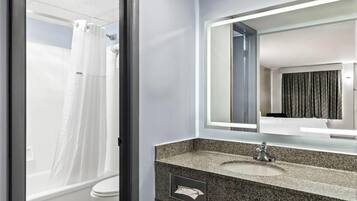 A bathroom with a white toilet, a granite sink, a mirror with a light, and a shower curtain.