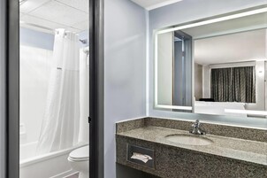 A bathroom with a white toilet, a granite sink, a mirror with a light, and a shower curtain.