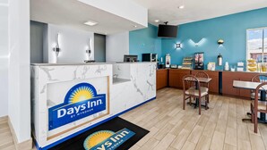 A Days Inn reception area with a marble counter, a TV mounted on the wall, and a dining area with wooden chairs and tables.