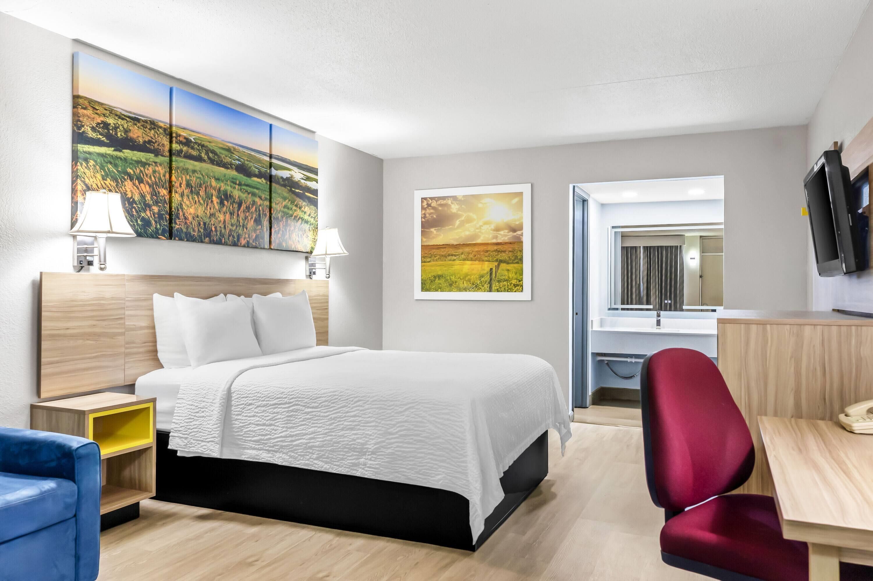 Habitación de hotel con cama, escritorio, silla, televisión y obras de arte en las paredes.