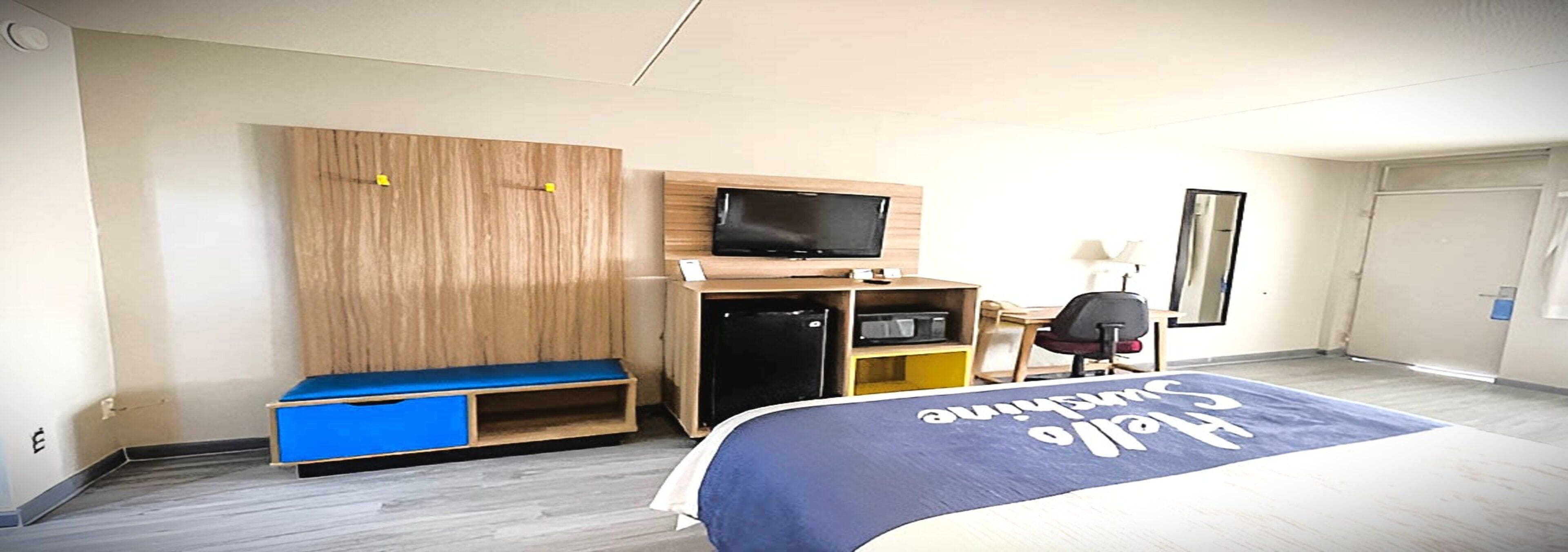 Una habitación de hotel con una cama, un escritorio con computadora, televisor y armario.