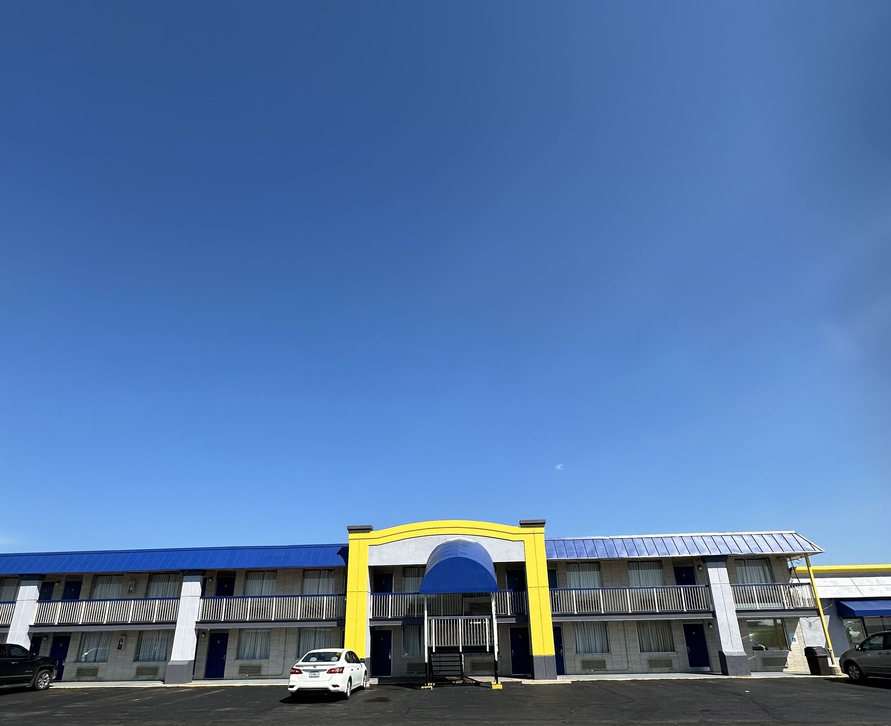A multi-story motel with a blue and yellow facade, a covered entrance, and a parking lot.