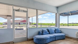A spacious room with large windows, a blue sectional sofa, and a view of a building and fields outside.