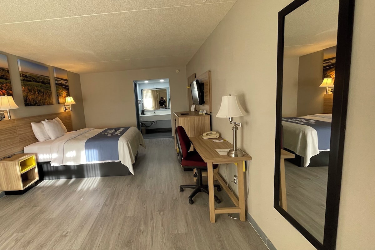 Une chambre d’hôtel équipée d’un lit, d’un bureau, d’une chaise et d’un grand miroir.