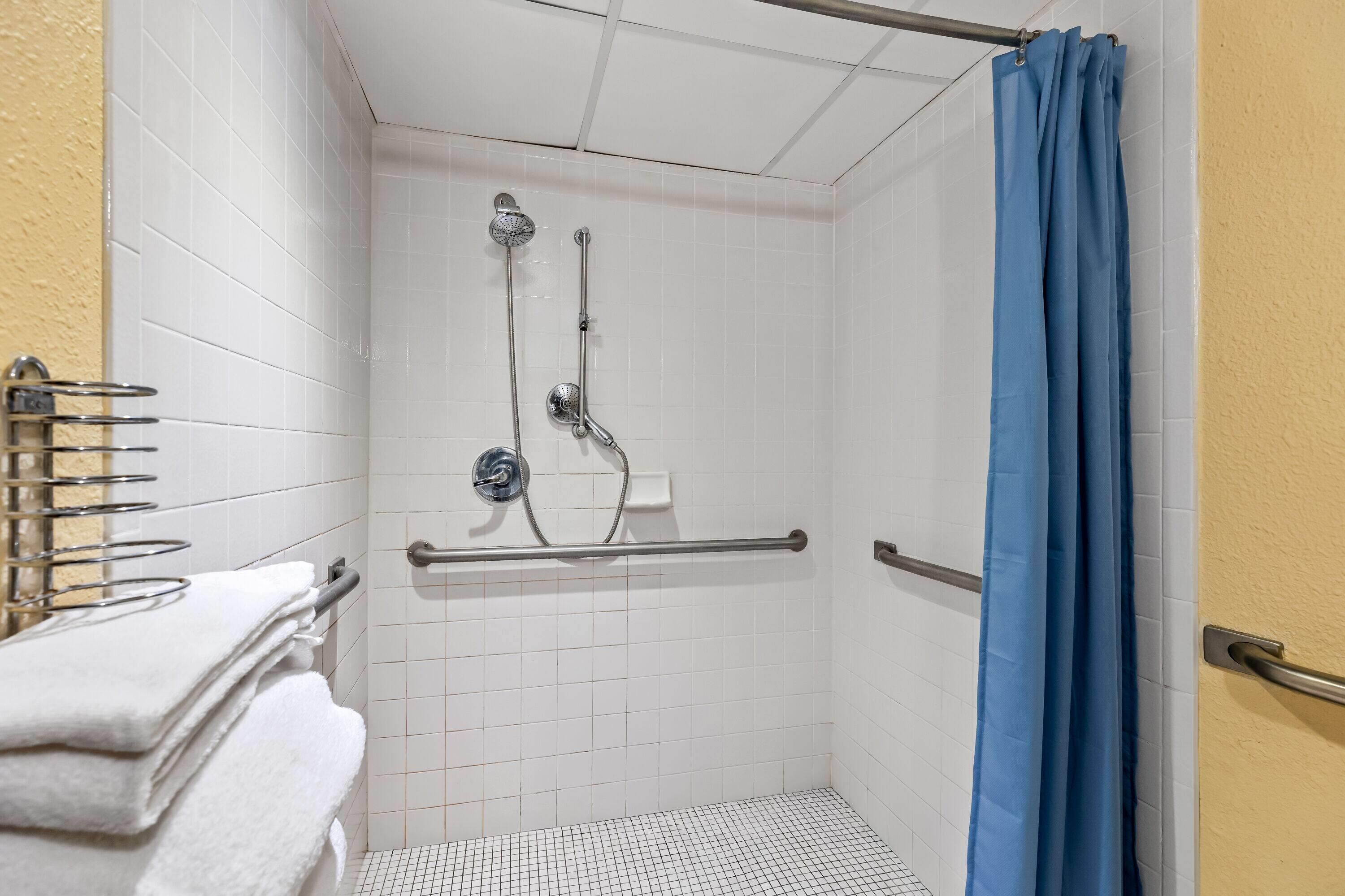Un petit espace de douche carrelé, avec un rideau de douche bleu, une barre d’appui et des serviettes pliées.