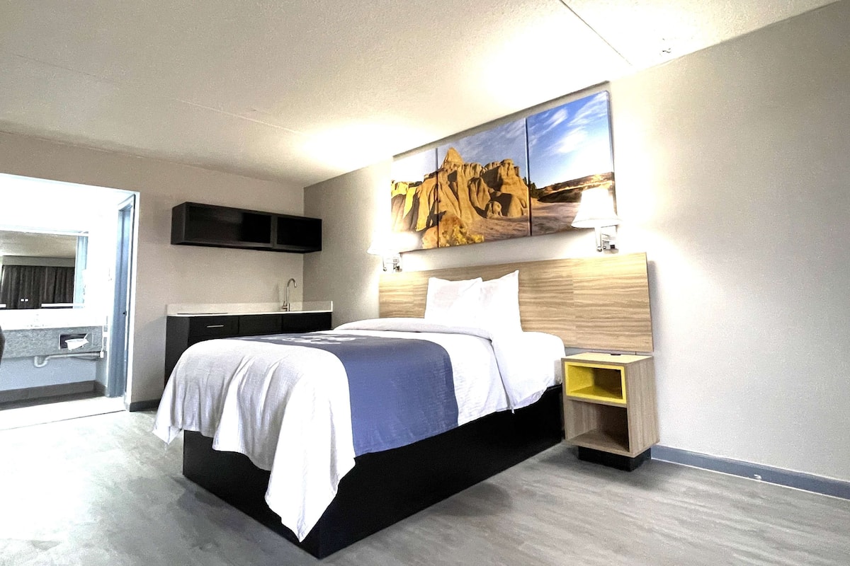 Une chambre d’hôtel moderne avec un grand lit, une tête de lit en bois, une table de chevet et un téléviseur fixé au mur.
