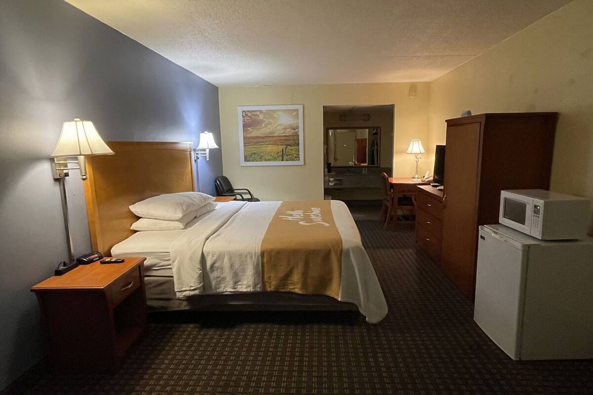 Une chambre d’hôtel équipée d’un lit, de lampes de chevet, d’un bureau avec une chaise, d’un four à micro-ondes et d’un réfrigérateur.