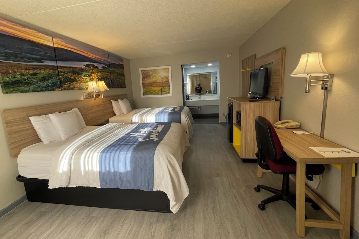 Une chambre d’hôtel avec deux lits, un bureau, une chaise, une télévision et un miroir.