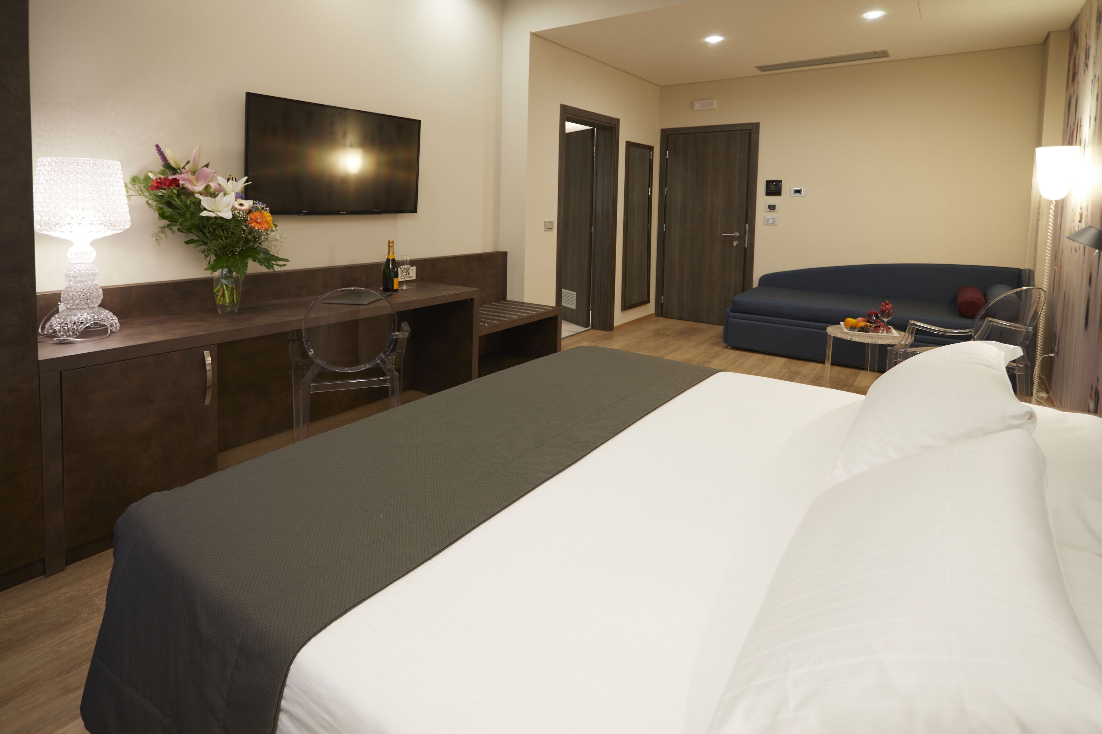 Ein Hotelzimmer mit einem Bett, einem Schreibtisch mit Lampe, einem Fernseher, einem Sofa und einem kleinen Tisch mit Obst.