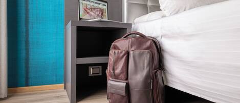 A neatly made bed with white linens, a brown leather backpack on the floor, and a laptop on a nightstand.