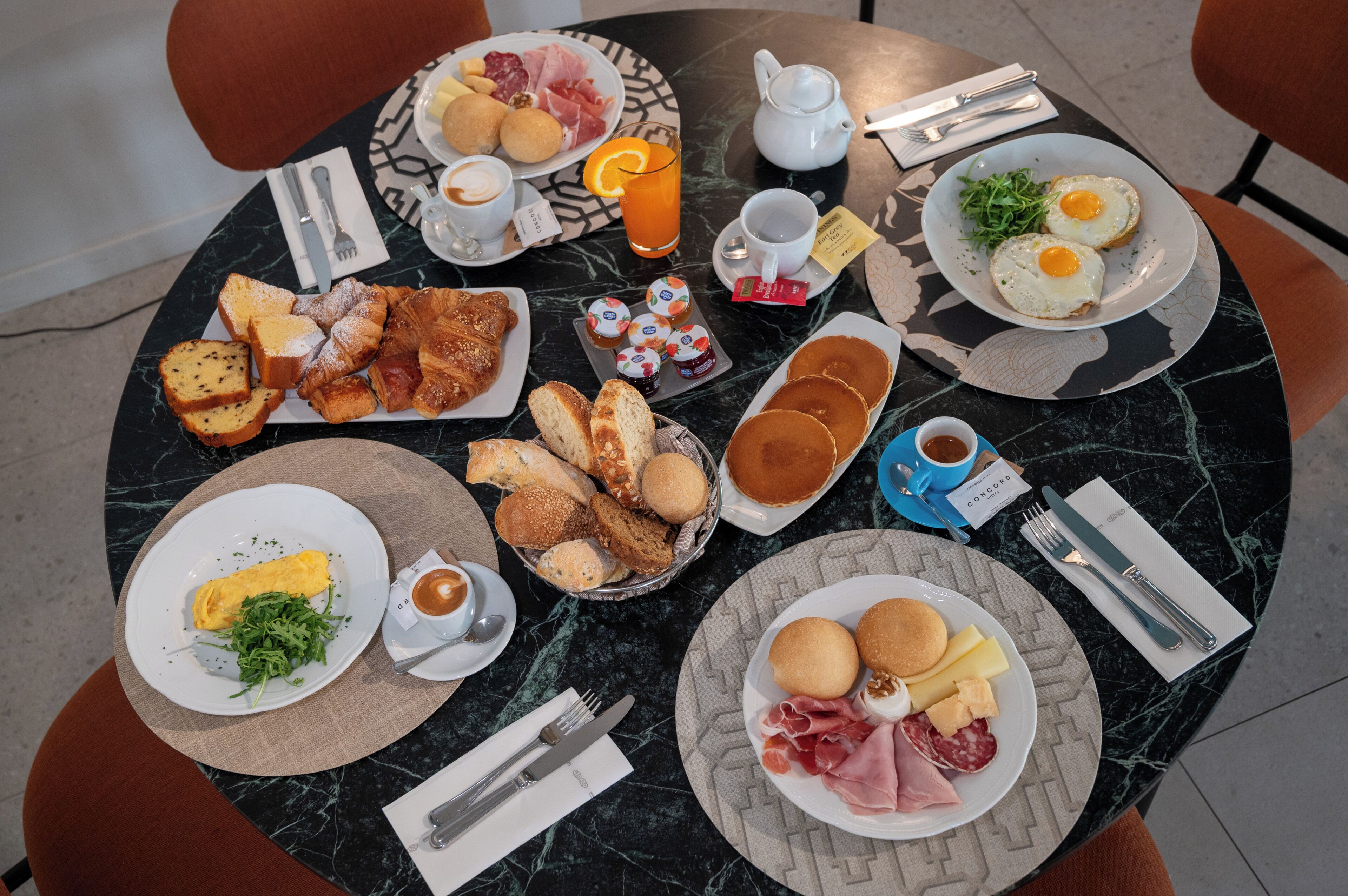 A breakfast setting with various dishes, a teapot, and cutlery on a marble table.