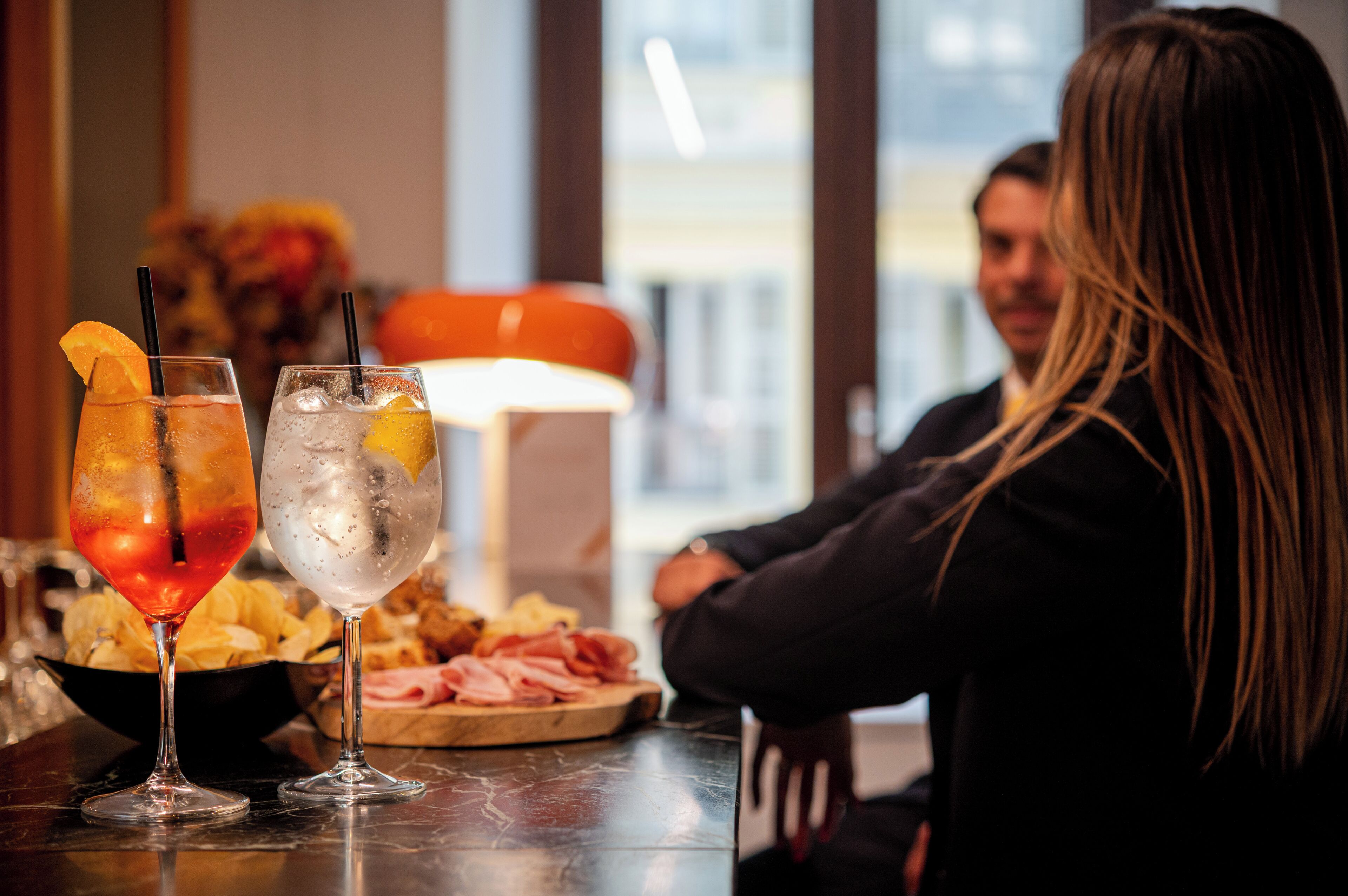 Un bar con dos bebidas, un cuenco de papas fritas y un plato de embutidos.