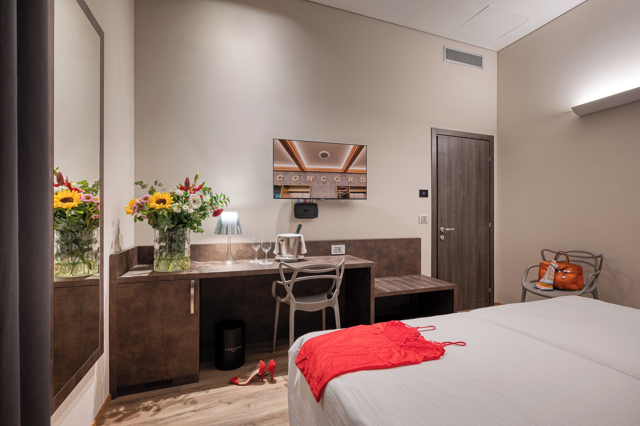 Habitación de hotel con cama, escritorio, silla, televisor y puerta.