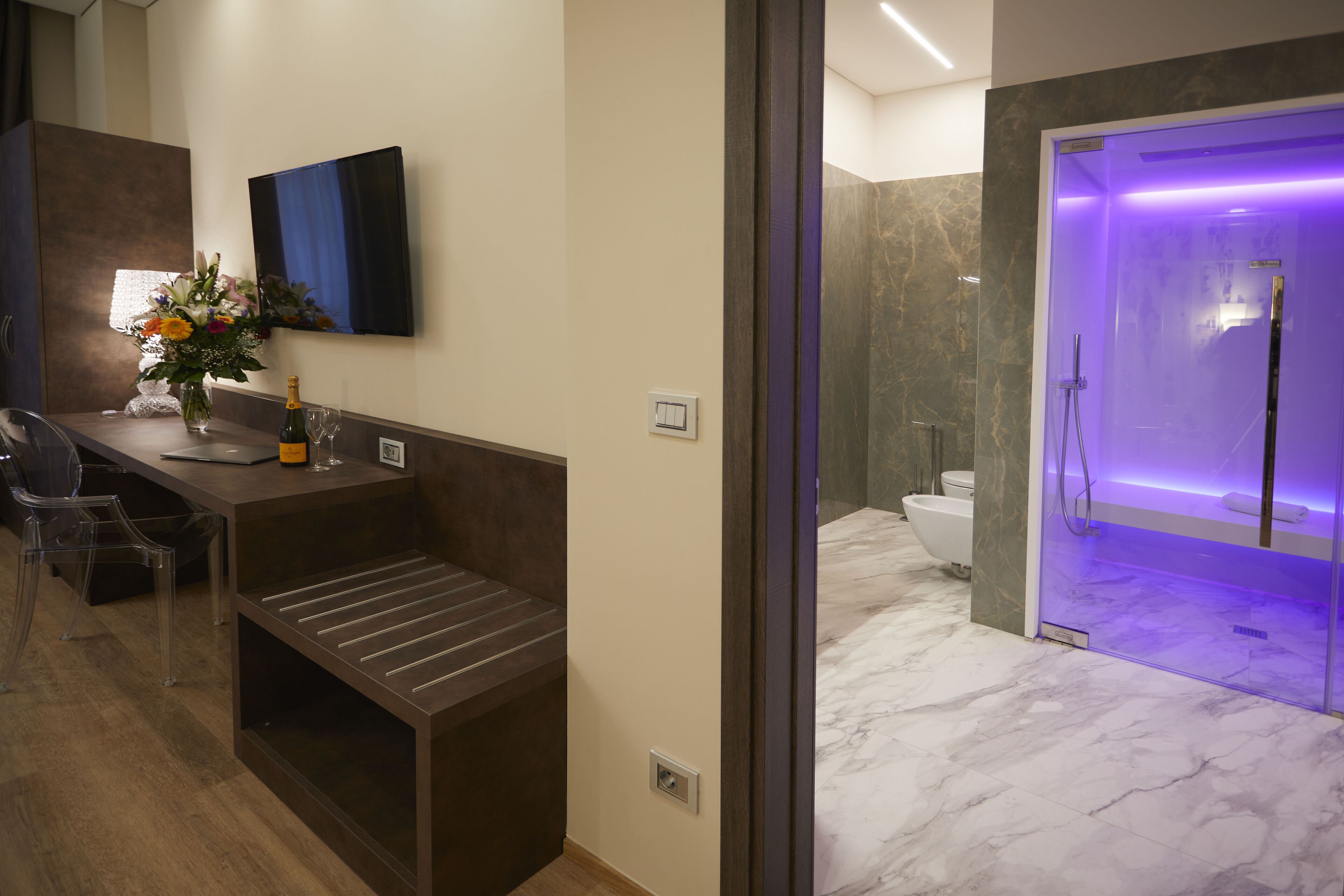 Une salle de bain moderne avec un sol en marbre, une douche en verre et un lavabo agrémenté d’un vase de fleurs.