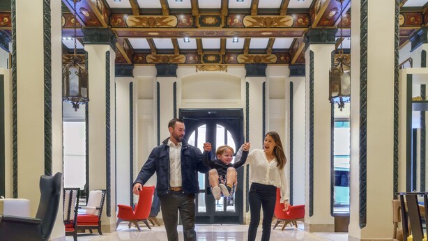 A family walking through a lobby with high ceilings, chandeliers, and modern seating.