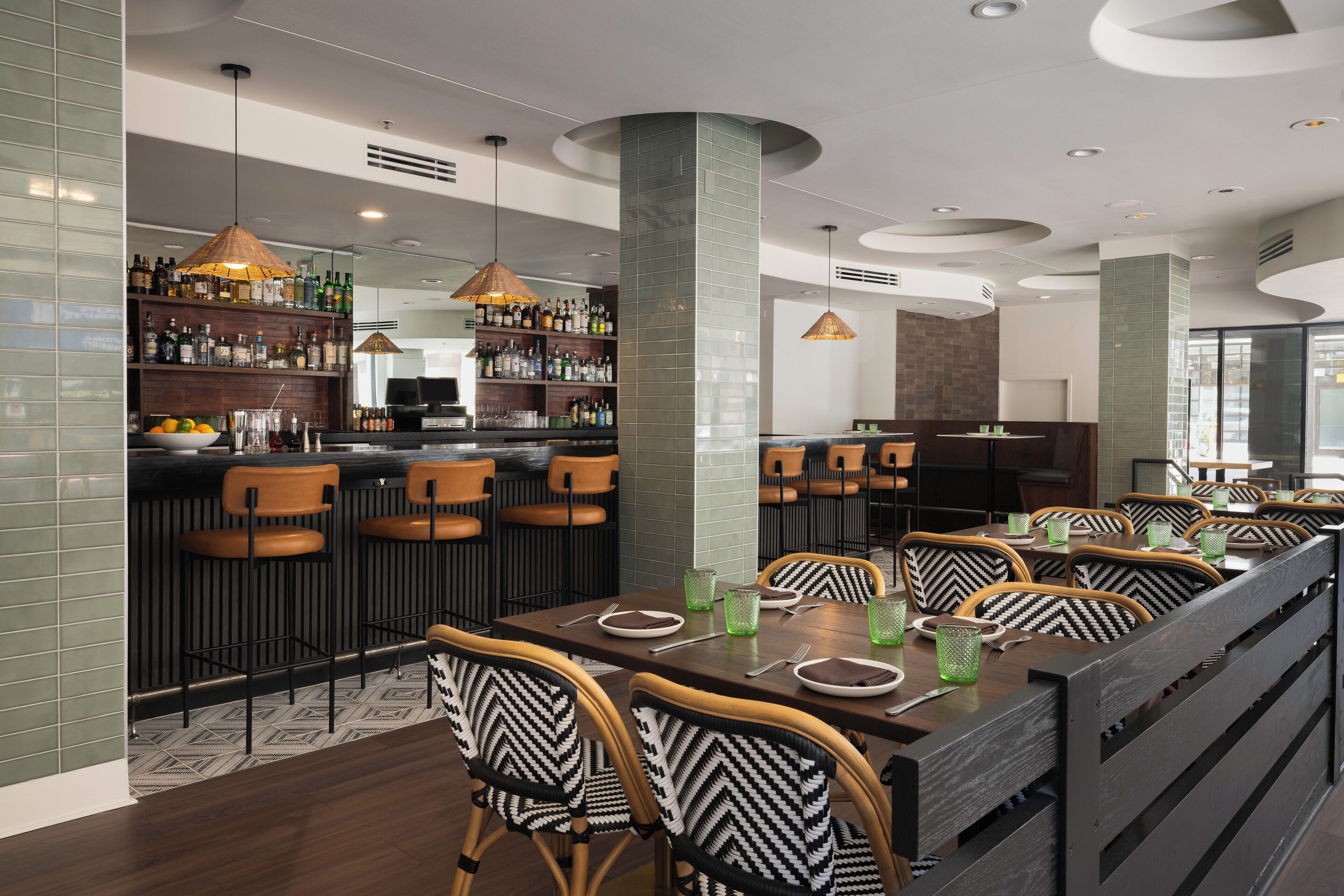 A modern bar area with a long counter, multiple seating options, and a variety of bottles on shelves.