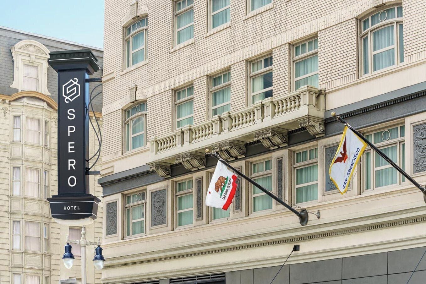 Un bâtiment d’hôtel avec une enseigne bien visible portant l’inscription « SPERO HOTEL » et des drapeaux indiquant qu’il se trouve à San Francisco.