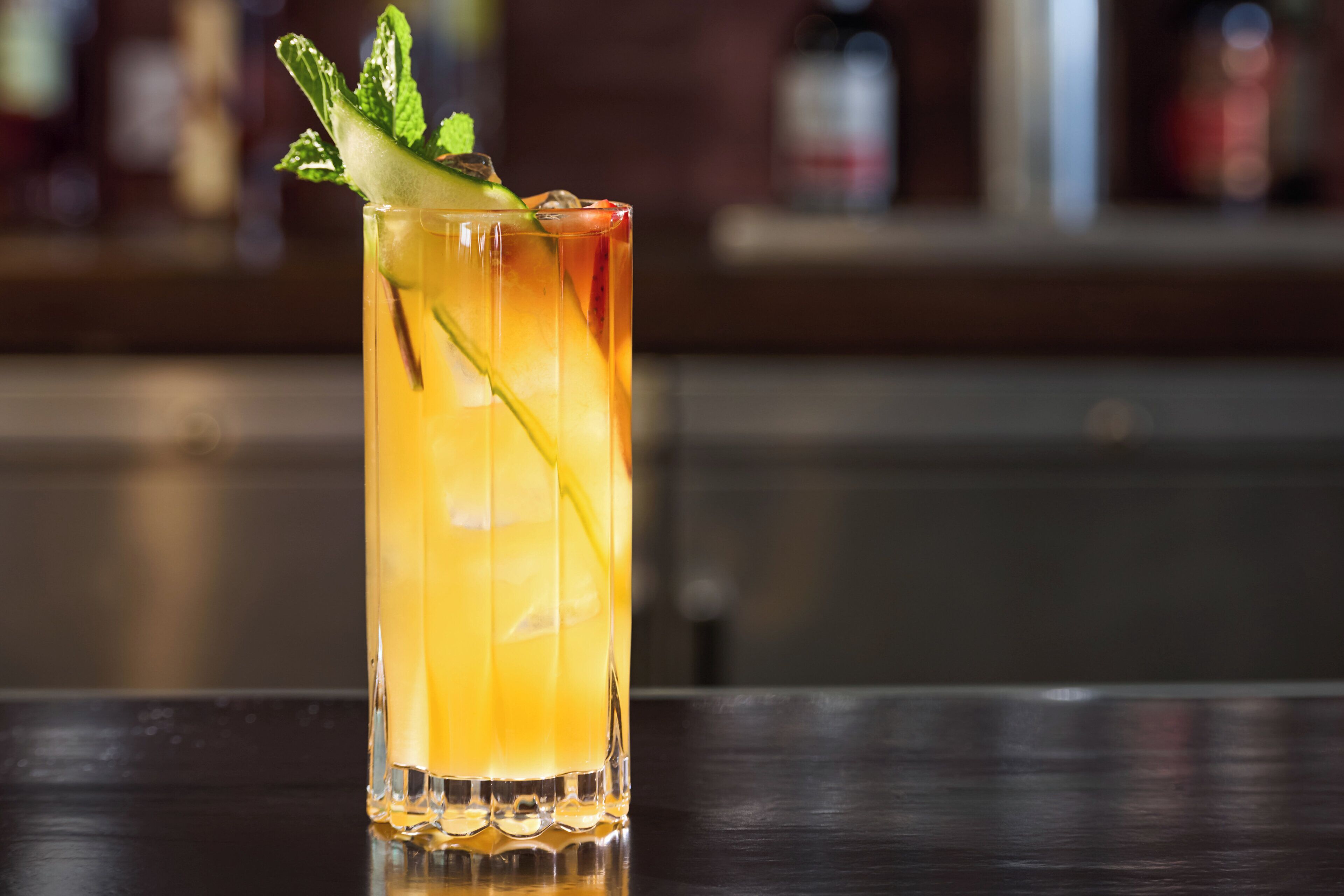 Un grand verre contenant une boisson, décoré de feuilles de menthe, posé sur une surface réfléchissante.